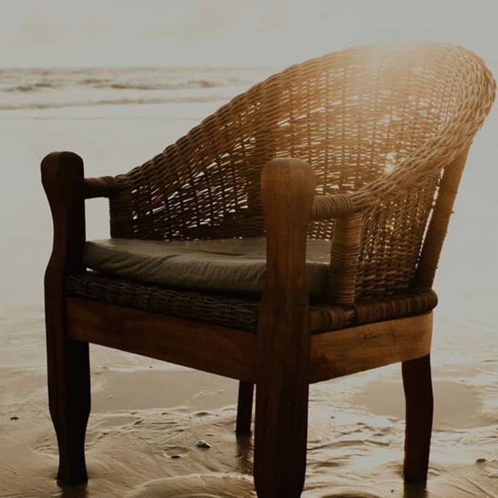 Illustration: Wood and cane chair on beach sand, with the sun rising just above it and the ocean in the background.