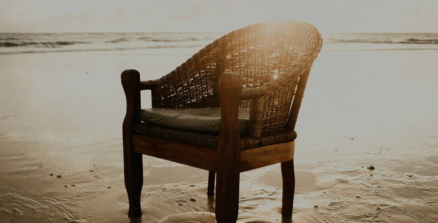 Illustration: Wood and cane chair on beach sand, with the sun rising just above it and the ocean in the background.